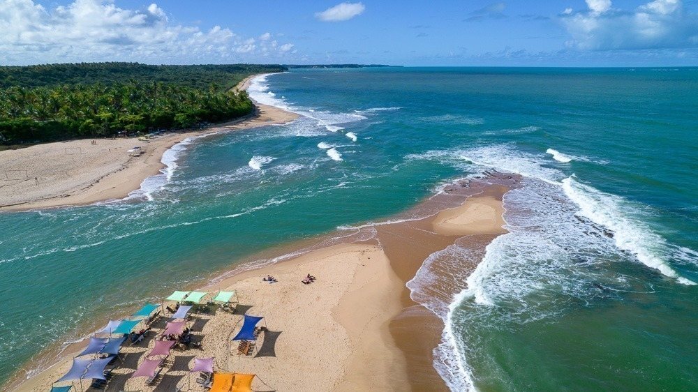 Guarda-sóis coloridos na areia e o banco de areia da Praia da Barra vistos de cima