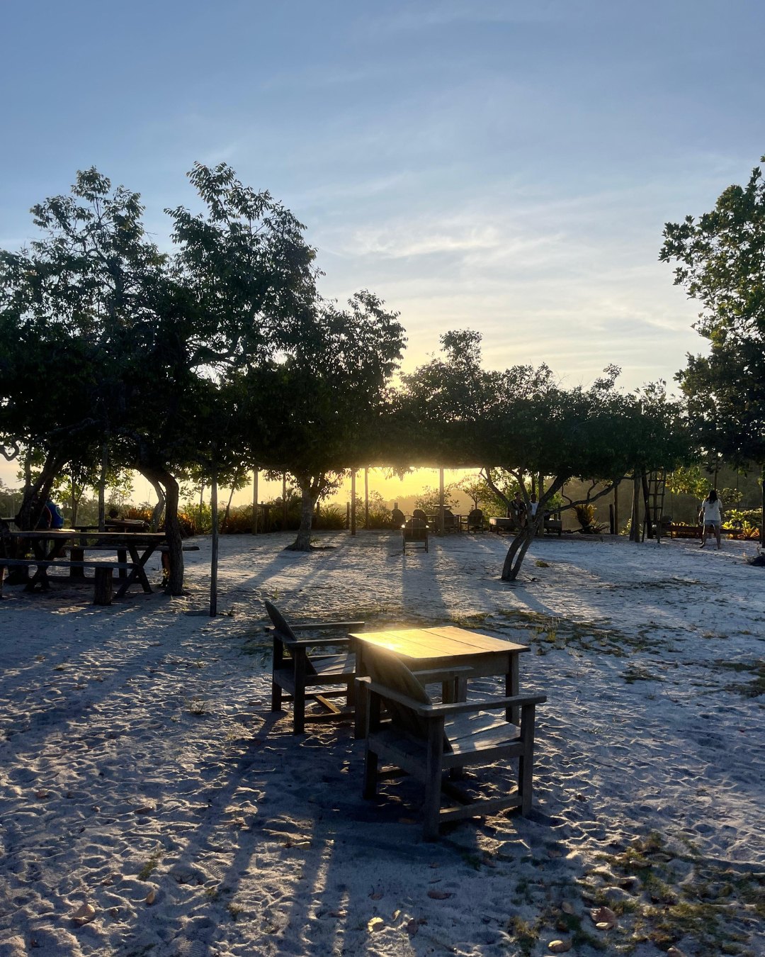 Mesas e cadeiras sob as árvores na estrutura da Prainha ao entardecer